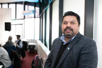 Man standing smiling at the camera in a room full of people